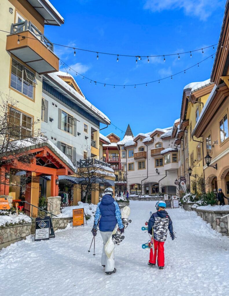 mother and son walking through ski village with snowboards in british columbia