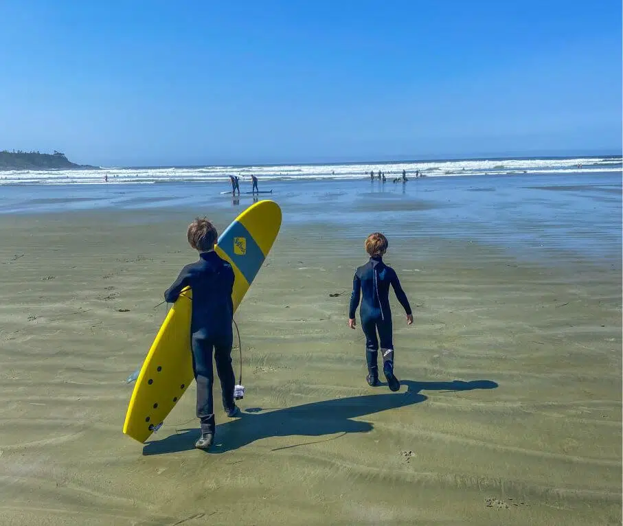 boys walking on beach with yellow surfboard